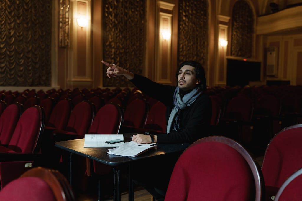 A theater director gestures in an empty auditorium during a rehearsal planning session.