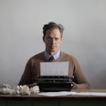 A thoughtful male writer typing on a vintage typewriter, surrounded by crumpled papers.
