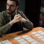 Man concentrating on organizing script cards on wooden table, symbolizing creative work and screenwriting.