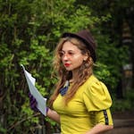 Stylish woman in vintage attire using a typewriter in a scenic outdoor setting.